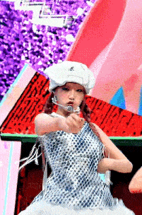 a woman in a white hat and a blue dress is pointing at the camera .