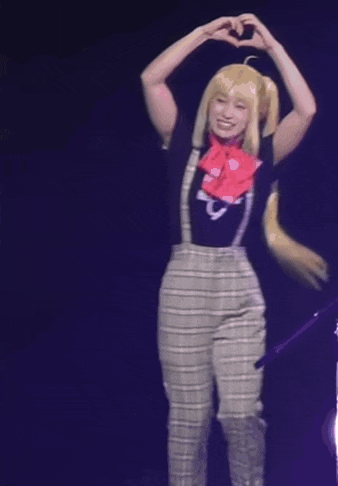 a woman making a heart shape with her hands while wearing suspenders