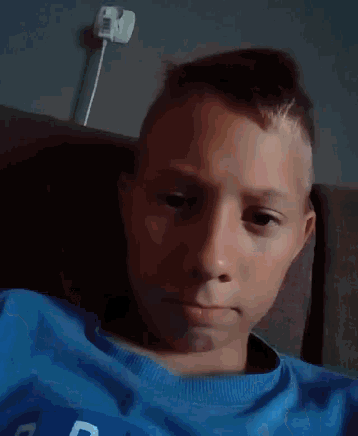 a young boy in a blue shirt is sitting on a couch