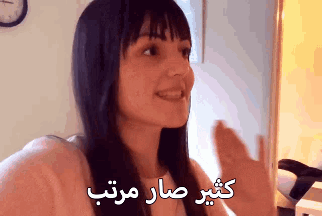a woman with a clock on the wall behind her with arabic writing