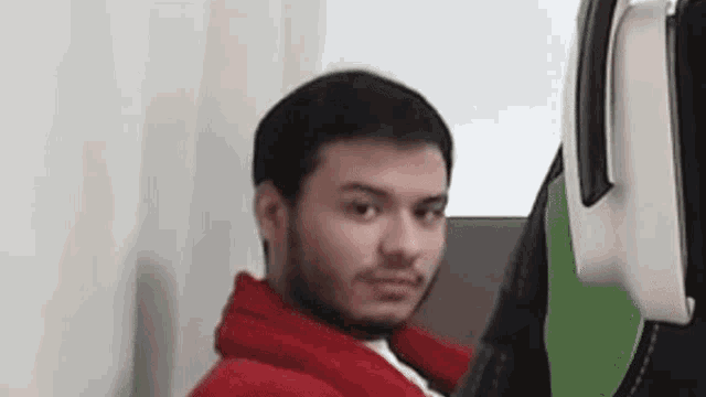 a man in a red hoodie is sitting next to a chair and making a funny face .