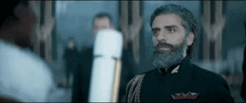 a man with a beard and a black uniform is standing in front of a group of people .