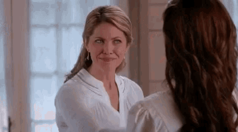 two women are standing next to each other and looking at each other in a mirror .