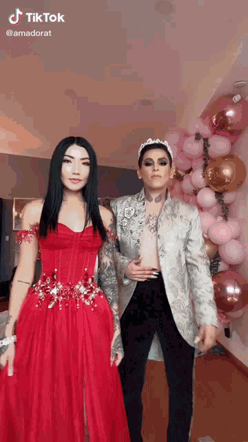 a woman in a red dress is standing next to a man in a silver jacket .