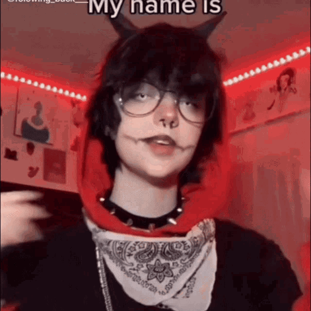 a person with horns and glasses is wearing a red hoodie and a bandana around their neck .