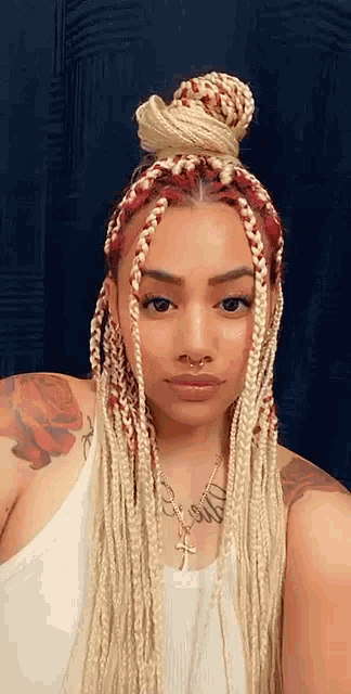 a woman with blonde and red braids is wearing a white tank top and a necklace .