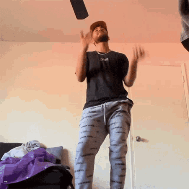 a man in a black shirt and grey sweatpants is dancing in a bedroom