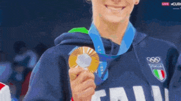a woman wearing a blue italia shirt holds a gold medal around her neck