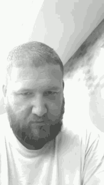 a black and white photo of a man with a beard wearing a white t-shirt .