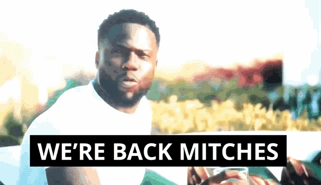 a man with a beard is sitting in front of a sign that says " we 're back mitches "