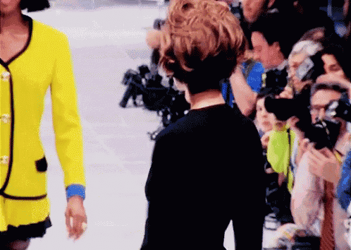 a woman in a yellow jacket is walking down the runway at a fashion show .