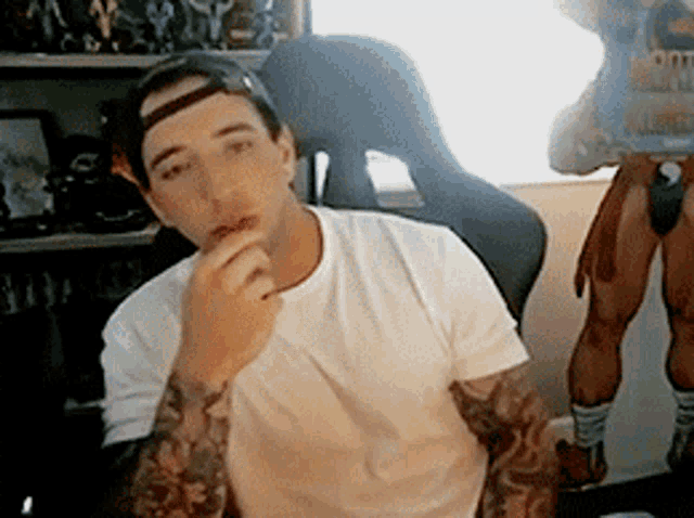 a man with tattoos on his arms is wearing a white shirt and a hat