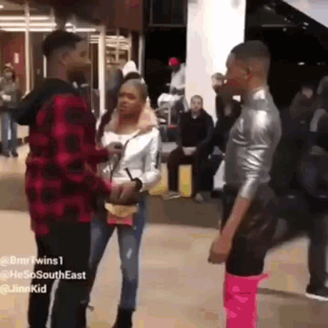 a man in a plaid shirt is talking to a woman in pink pants in a crowded room .