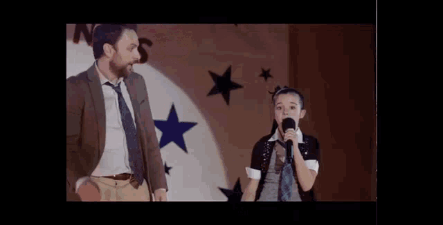 a little girl singing into a microphone with a man standing behind her