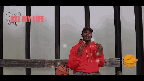 a man in a red hoodie is sitting on a bench with a basketball in front of a window .