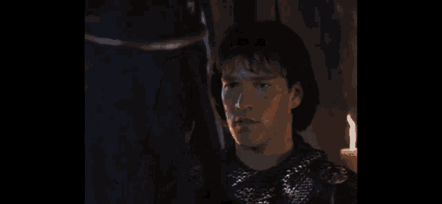 a man in a knight 's armor is standing in a dark room with a candle .