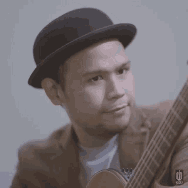 a man wearing a hat and a suit is holding a guitar .