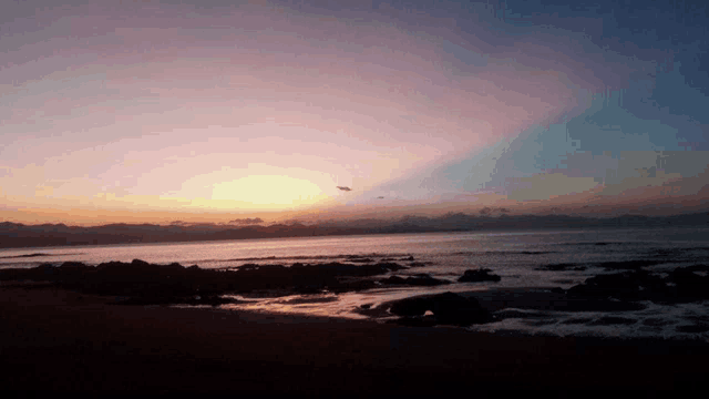 a sunset over a body of water with a plane flying in the distance