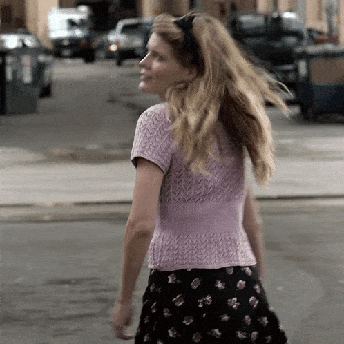 a woman wearing a purple top and black skirt is walking down the street