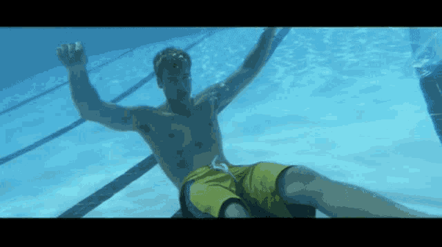 a shirtless man in yellow swim trunks is swimming underwater