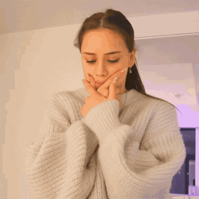 a woman wearing a grey sweater is making a face with her hands