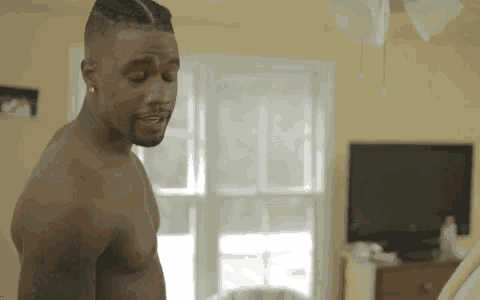 a shirtless man is standing in a living room in front of a window .