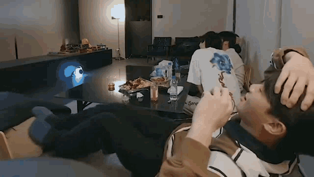 a group of people are sitting around a table in a living room with a projector .