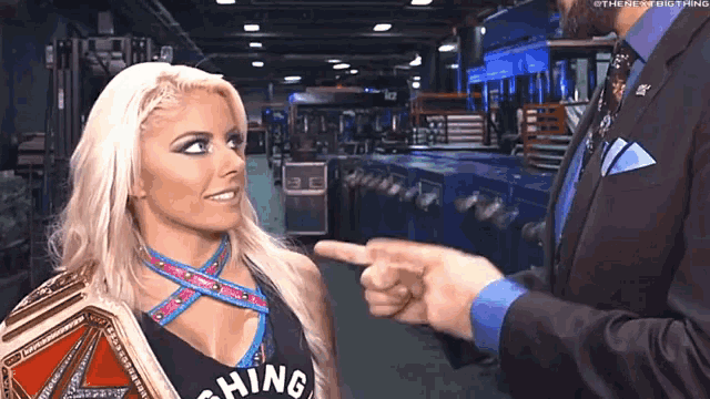 a man in a suit and tie is pointing at a woman in a wrestling ring .