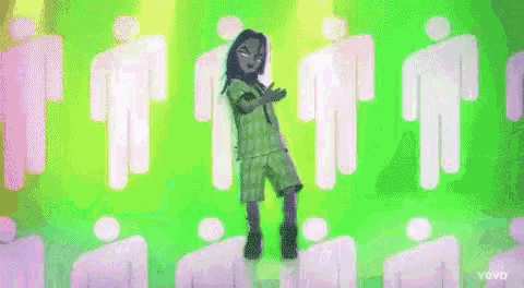 billie eilish is standing in front of a green background with a bunch of cartoon people .