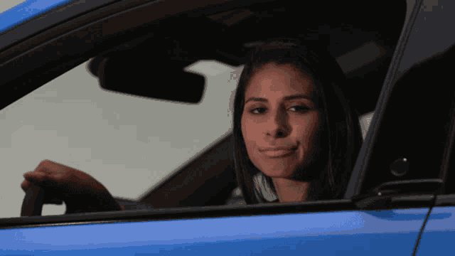 a woman in a blue car looks out the window and smiles