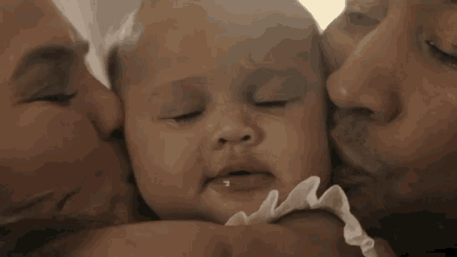 a man and woman are kissing a baby on the forehead .