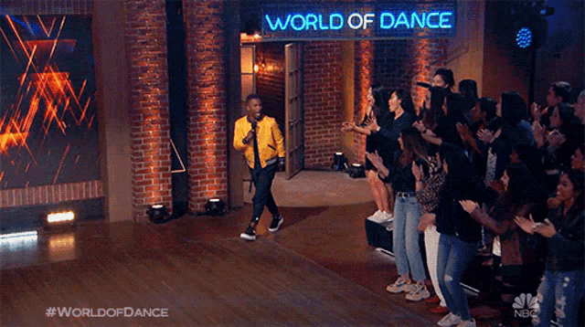 a man in a yellow jacket is standing in front of a crowd of people under a world of dance sign