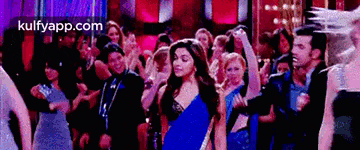 a woman in a blue saree is dancing in a crowd of people .