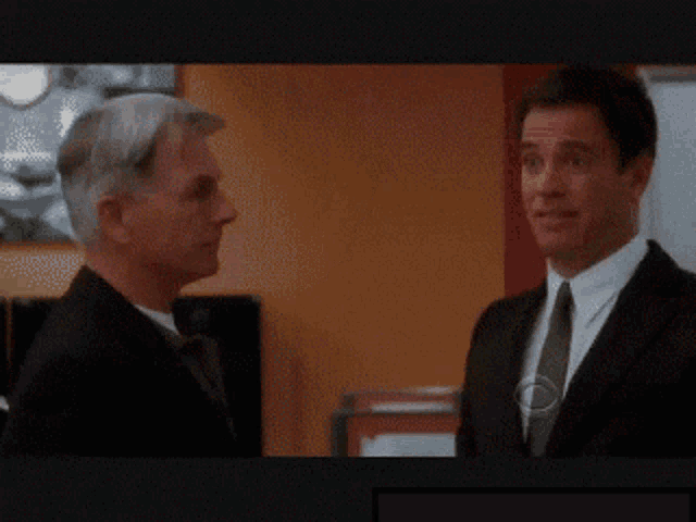 a man in a suit and tie talks to another man in a suit