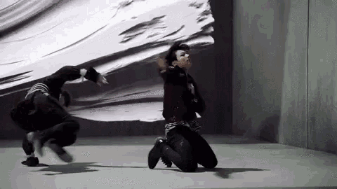 a man is kneeling down in front of a wall while another man is jumping in the air .