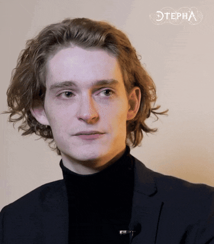 a young man in a suit and black turtleneck stands in front of a wall with the word stepha on it