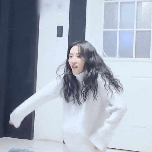 a woman wearing a white sweater is dancing in front of a door