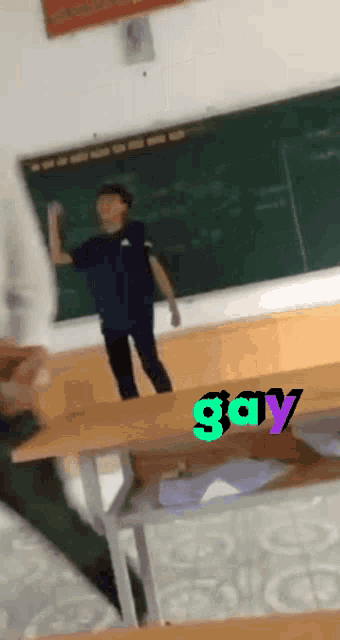 a man is standing on a desk in front of a blackboard with the word gay written on it