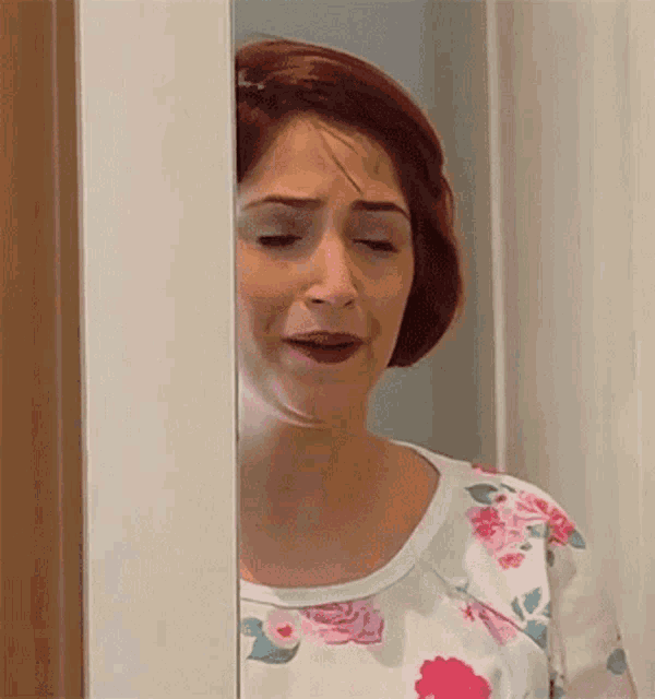 a woman with red hair is peeking out from behind a door .