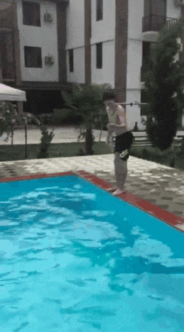 a man jumps into a swimming pool with a building in the background