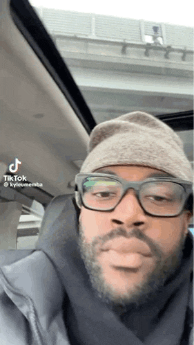 a man with glasses and a beanie is sitting in a car .