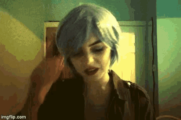 a woman with blue hair and red lipstick is looking at the camera .