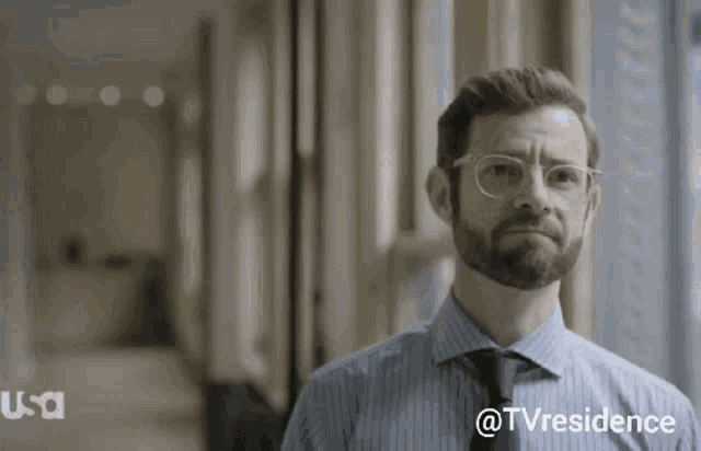 a man with glasses and a beard is standing in a hallway with a usa logo in the corner