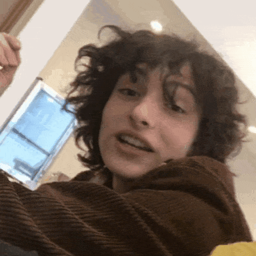 a young man with curly hair is taking a selfie in front of a mirror .