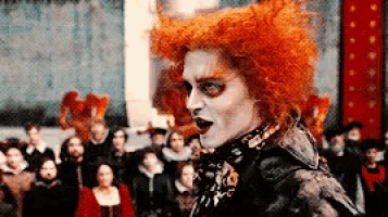 a man with red hair and white paint on his face stands in front of a crowd .