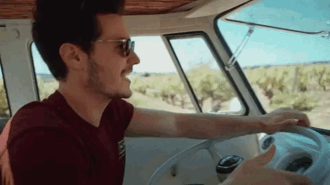 a man wearing sunglasses and a maroon shirt is driving a van