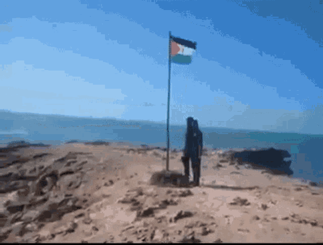 a person standing on top of a sandy hill next to a flag .