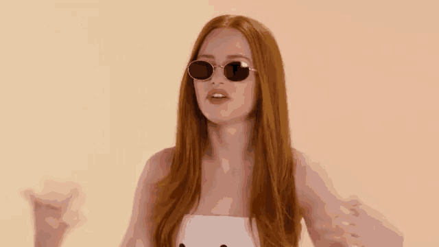 a woman with long red hair is wearing sunglasses and a white top .