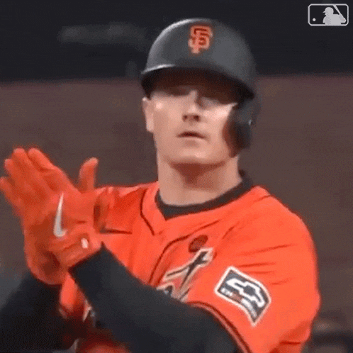 a baseball player wearing a helmet and gloves is clapping his hands in the air .