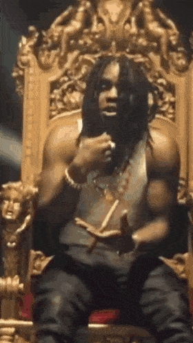 a man with dreadlocks is sitting on a throne eating a sandwich .